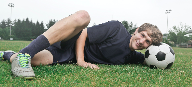 A football player laying in the grass with a ball under his head during football coaching in uae. 