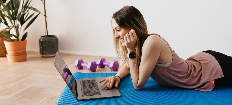 A Woman browsing a laptop on a yoga mat. 