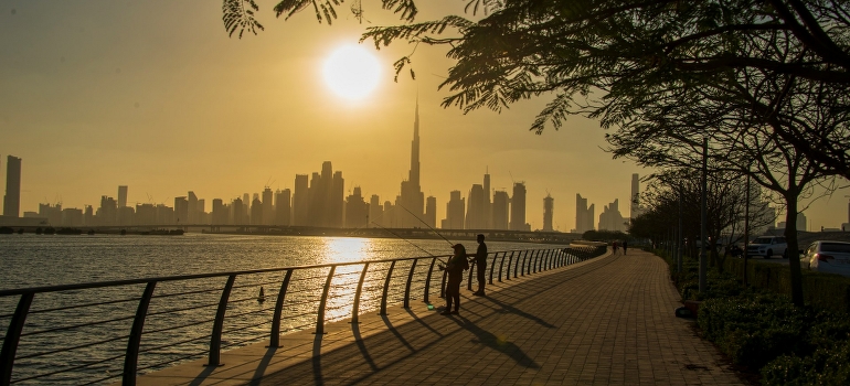 A group of people is standing by the sidewalk during sunset in Dubai. 