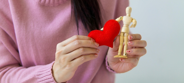 A woman holding a heart and a wooden doll after finding out how physical activity in UAE helps with chronic diseases.