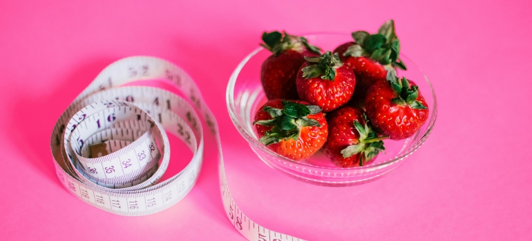 A ball of strawberries next to a measuring tape. 