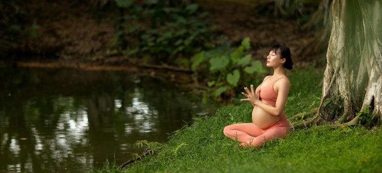 A pregnant woman meditating in the forest.
