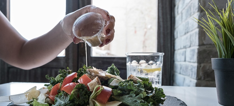A woman pouring a dressing on her salad. 