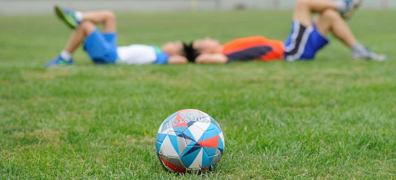 Two boys laying in the field with a ball in front of them wondering how Football Contributes to Overall Fitness