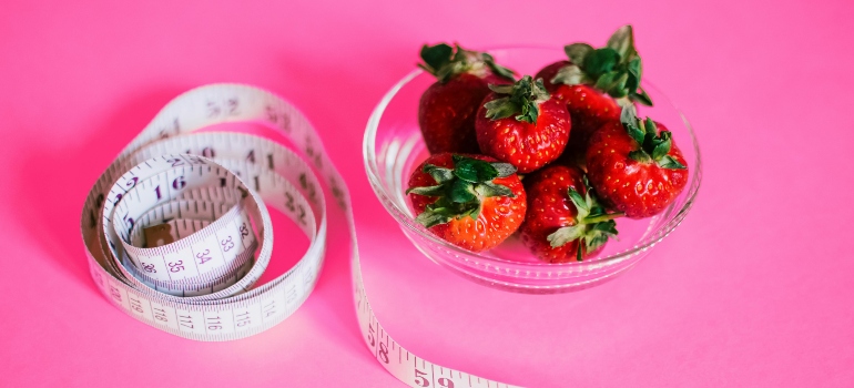 a bowl of strawberries next to a measuring tape.