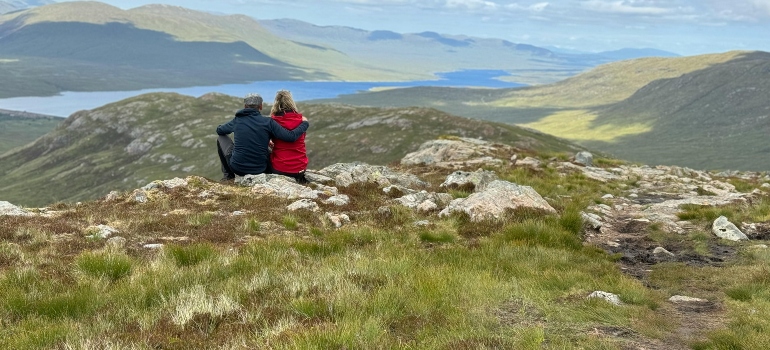 Two people sitting on a hill overlooking a lake and talking about best outdoor activities for fit couples.