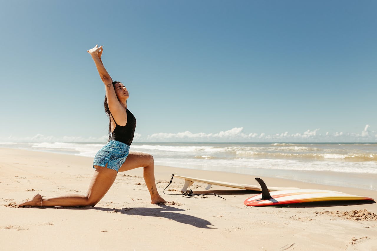 A woman stretching on a beach in Dubai next to a surfboard