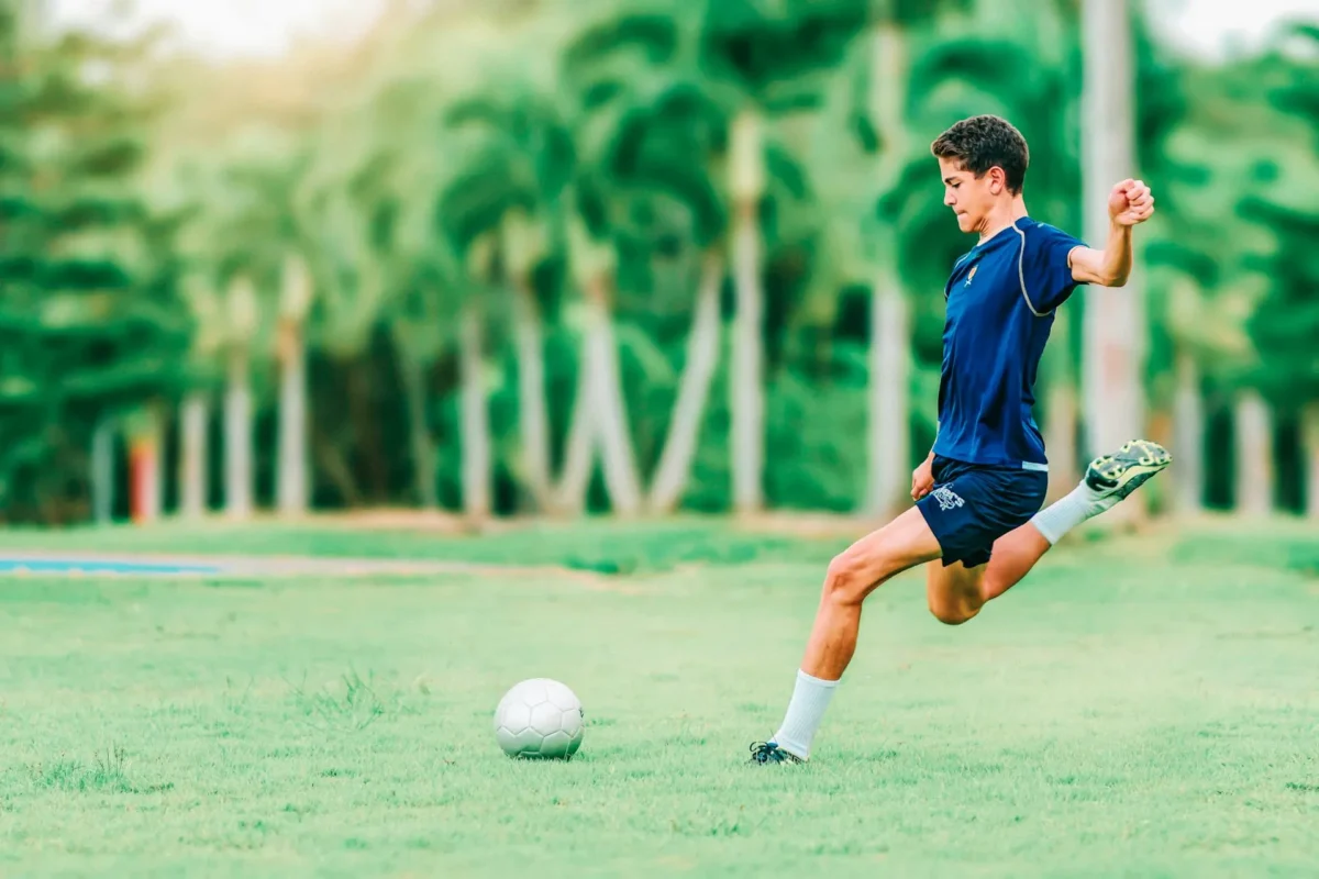 A man is trying to kick a soccer ball while thinking about the role of strength training in football.