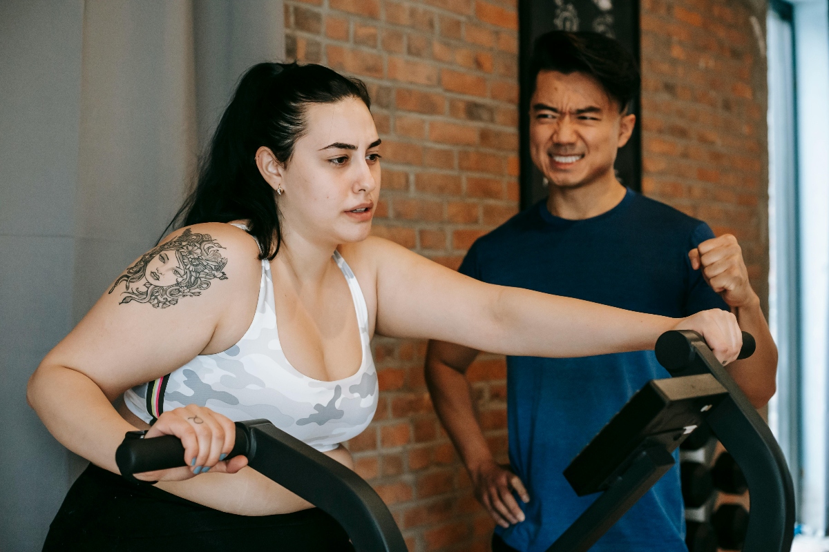 young woman training on elliptical machine with support of male instructor