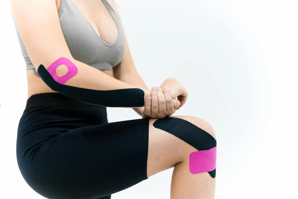 Woman in a black sports bra and leggings wearing stretchy support patches on her arm and leg, showing how to train after a minor injury without making it worse.