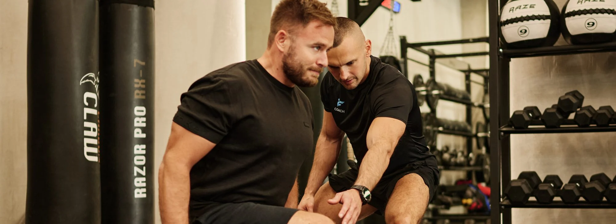 Nikola, male personal trainer, coaching a client's weighted lunge next to boxing bags in a Dubai gym