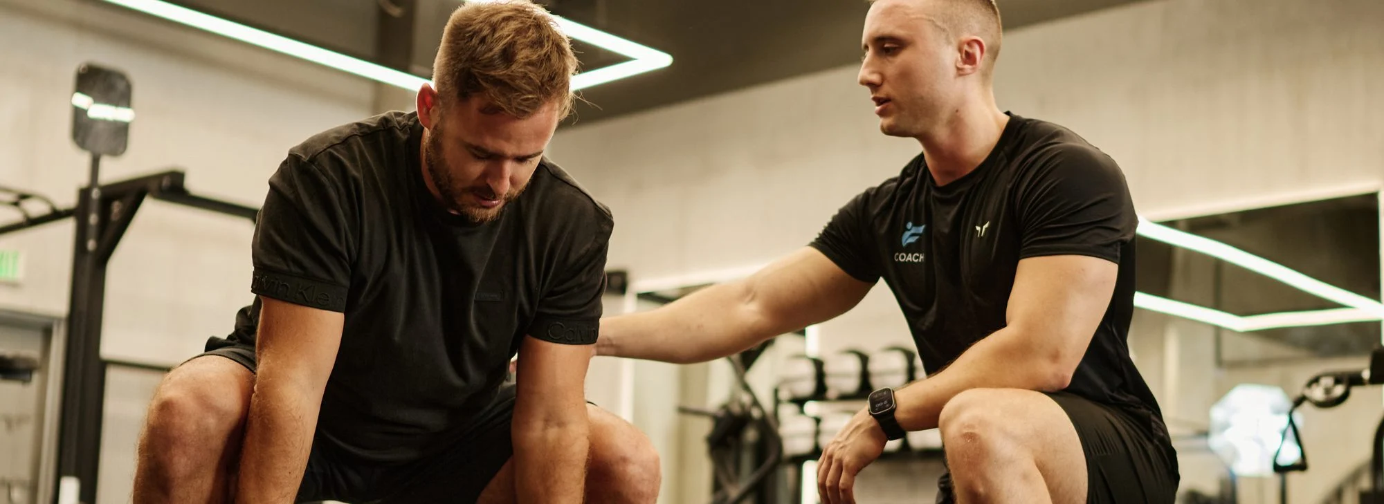 Tony, personal trainer, kneeling beside a client during a plate exercise in a Dubai gym
